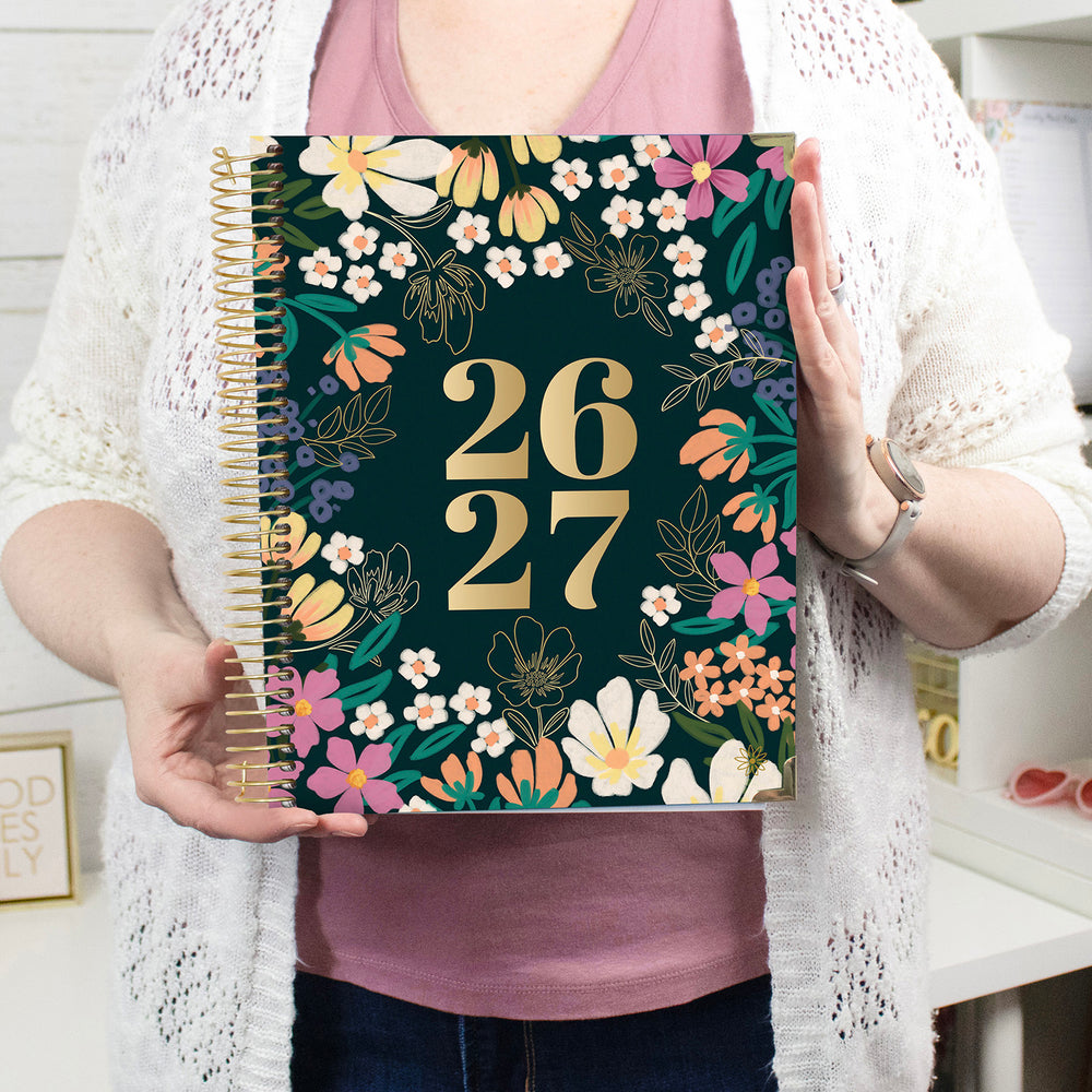 Person holding a planner with floral design and '26 27' text