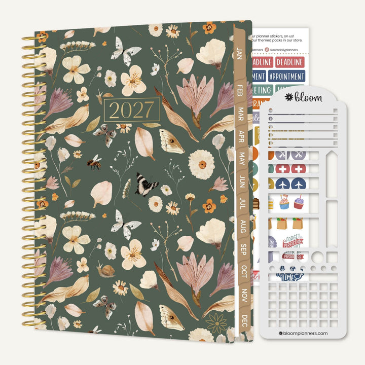 A 2027 spiral-bound planner with a muted green floral and bird patterned cover, shown with a white sticker sheet accessory on a light beige background. The planner cover features a gold-toned spiral binding, a gold '2027' plaque, and a vertical tab with monthly labels.