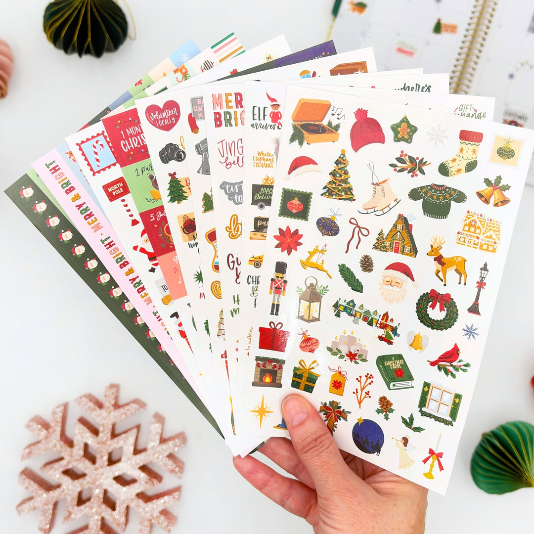 Hand holds Christmas planner sticker sheets with colorful holiday icons