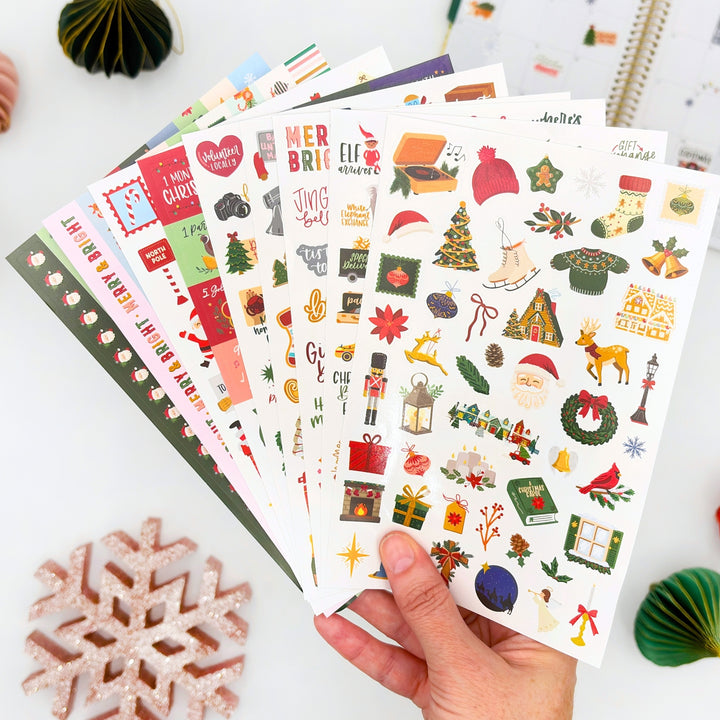Hand holds Christmas planner sticker sheets with colorful holiday icons