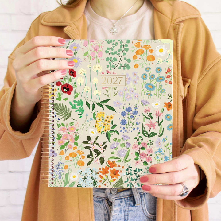 Person holding a floral-patterned planner with '2026-2027' on a white background