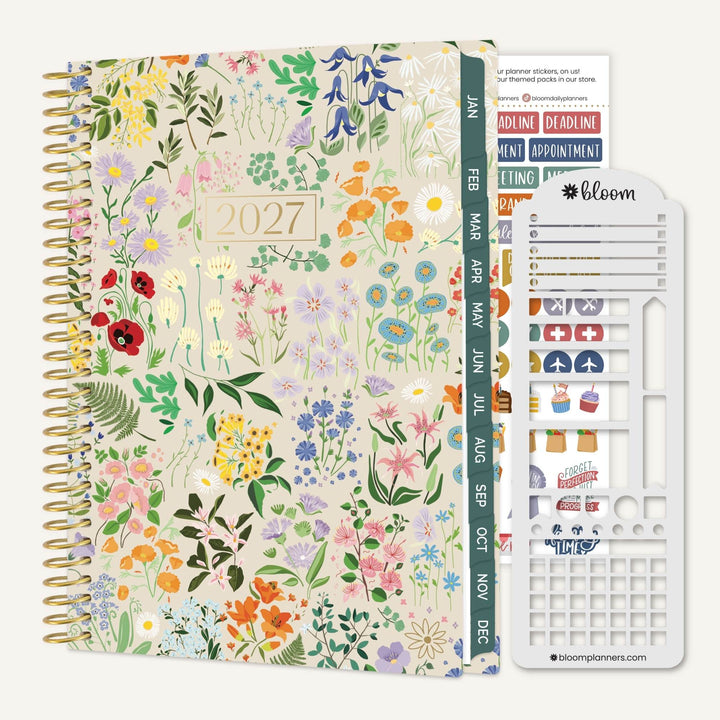 A 2027 spiral-bound planner with a dense multicolor floral and botanical print on the cover, shown alongside a white sticker sheet and a green monthly tab strip. The brand name 'bloom planners' is visible on the sticker sheet.