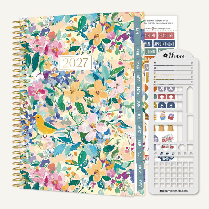 A 2027 spiral-bound planner with a colorful floral and bird patterned cover, shown with a white sticker sheet and divider tabs on a light neutral background. The brand name 'bloom planners' is visible on the sticker sheet.