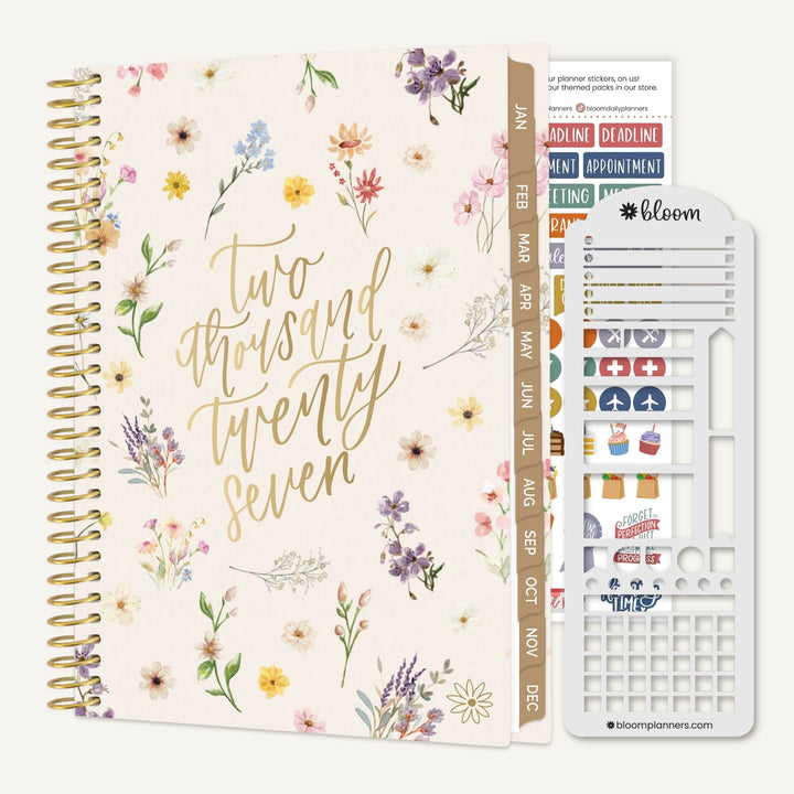 A floral planner set shown on a light neutral background, including a spiral-bound planner with gold lettering reading 'Two thousand twenty seven' and watercolor flowers, matching date strips, and a white sticker sheet labeled bloom.