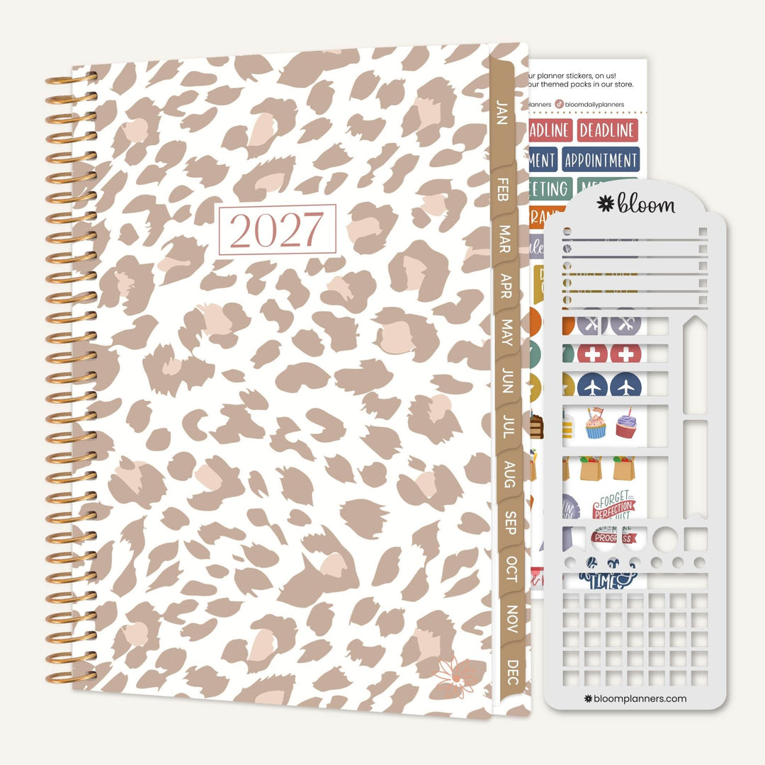 A 2027 spiral-bound planner with a beige and brown leopard print cover, shown with its included sticker sheet and tab strip on a light gray background.