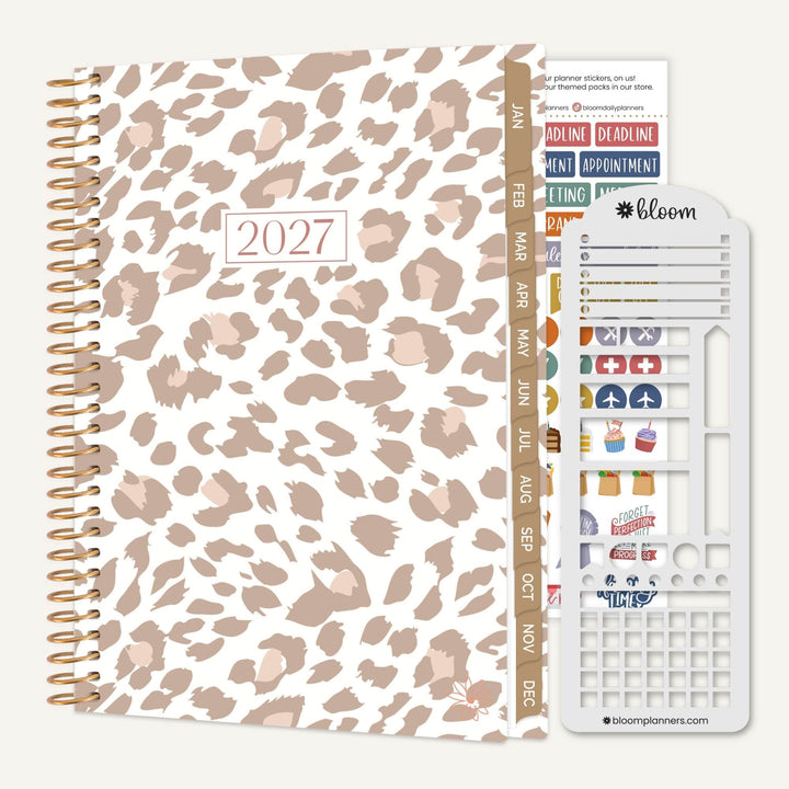 A 2027 spiral-bound planner with a beige and brown leopard print cover, shown with its included sticker sheet and tab strip on a light gray background.