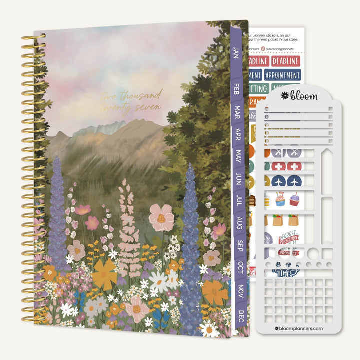 A spiral-bound planner or journal with a floral mountain landscape cover, shown next to a white sticker sheet and a vertical planner tab strip. The cover features pastel flowers, trees, and mountains with the text 'thousand and seven hundred and seventy seven'.