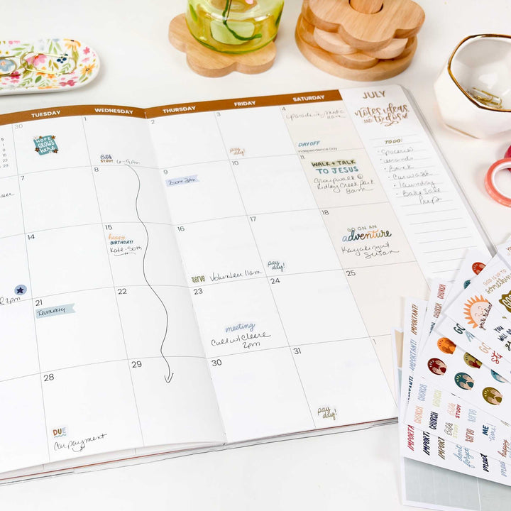 A pretty desk scene with a planner decorated with christian themed stickers. 