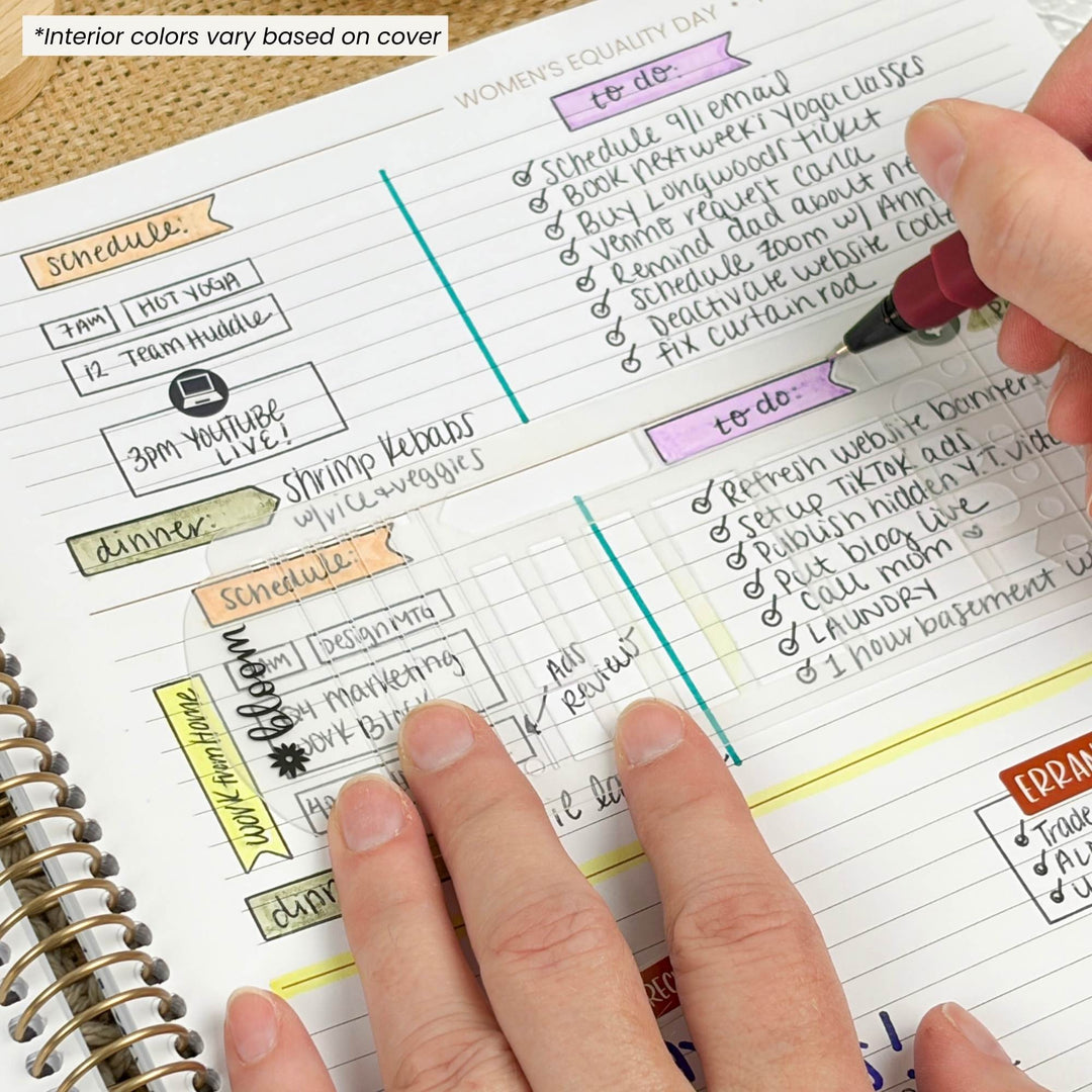 A close-up of a spiral-bound planner or notebook page with lined sections and colorful handwritten notes, with a hand holding a pen and another hand pointing at the page. A small text note in the top left says 'Interior colors vary based on cover.