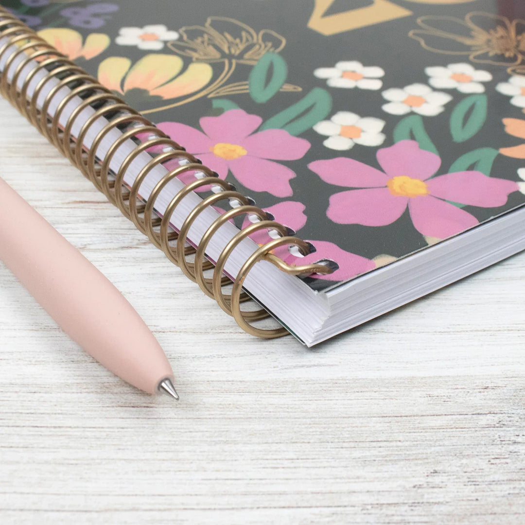 Planner with floral design on cover and a pen on a light wooden surface