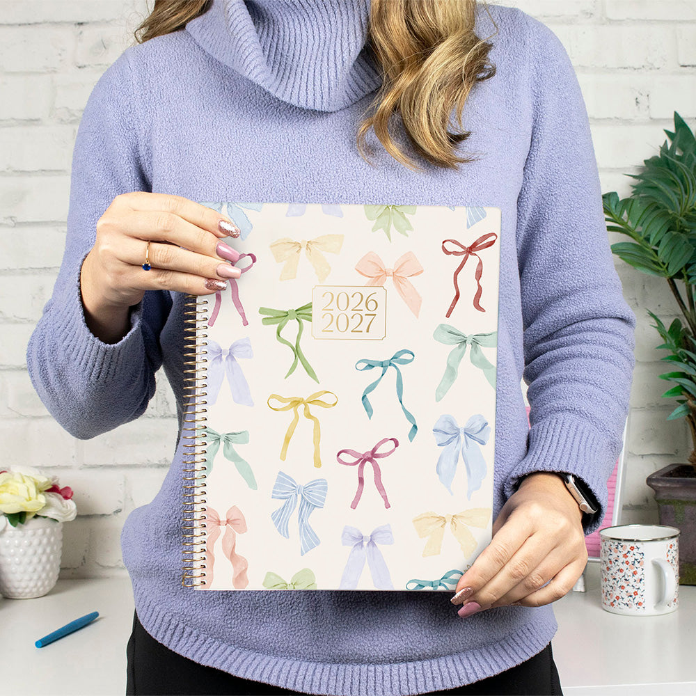 Woman holding a large academic planner with a bow motif. 
