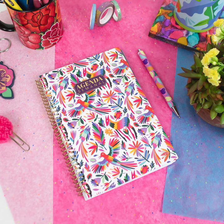Colorful agenda with floral design on a pink surface with stationery items.