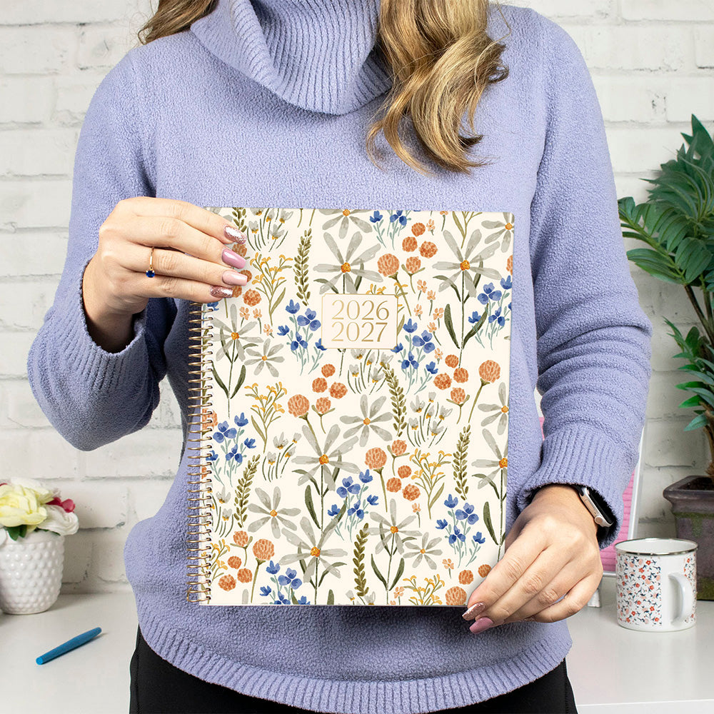 Person holding a floral-patterned planner with a white brick wall background