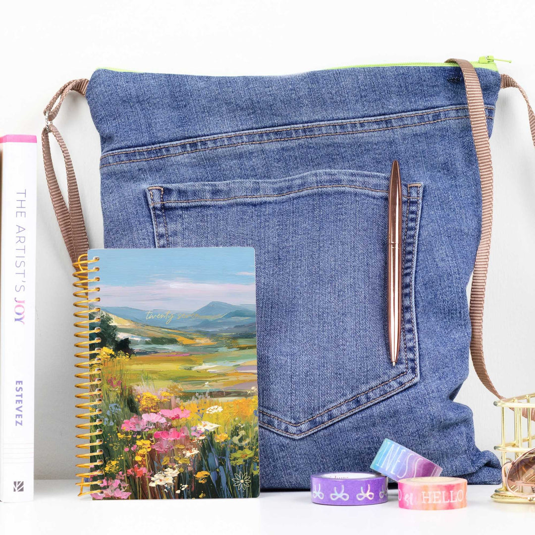 Blue denim bag with knitting needles and a notebook on a white background