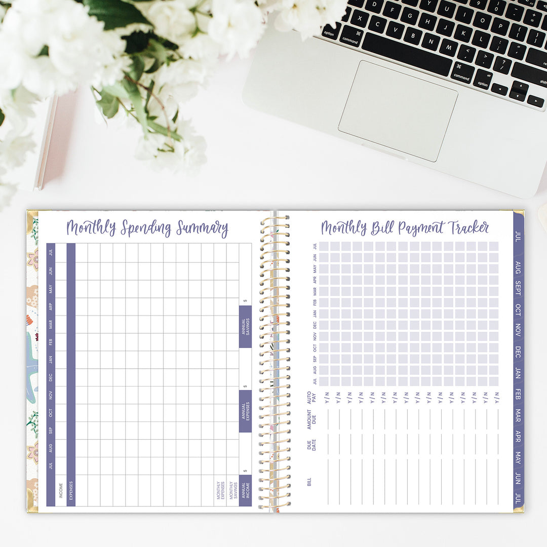 Open planner showing monthly spending summary and bill payment tracker pages, with a laptop and flowers in the background.