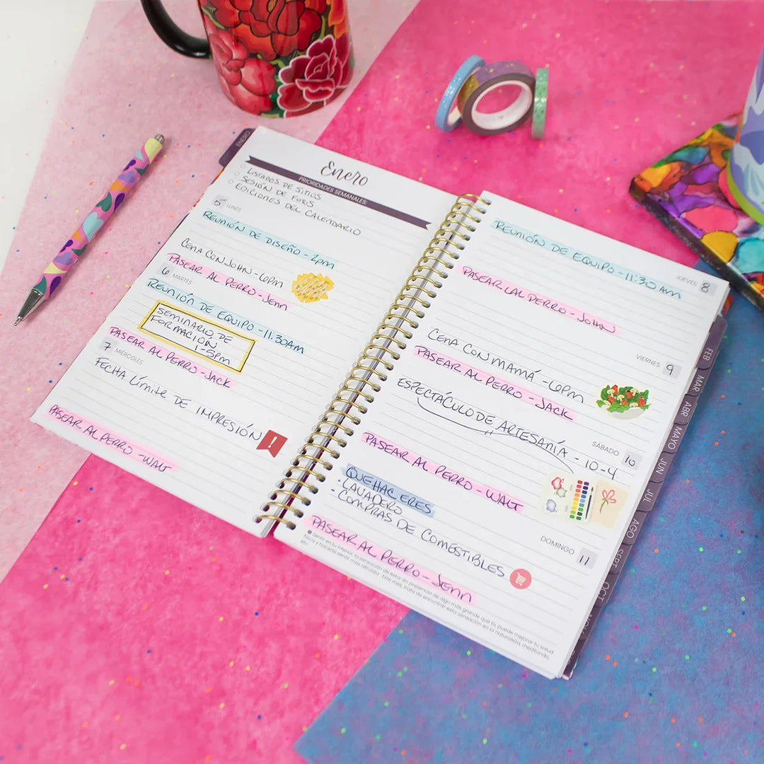 Open spiral-bound notebook with colorful notes on a pink and blue surface with stationery items.