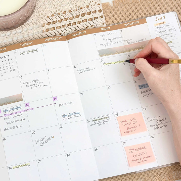 Person using a red pen to mark dates on a planner with July and August sections.