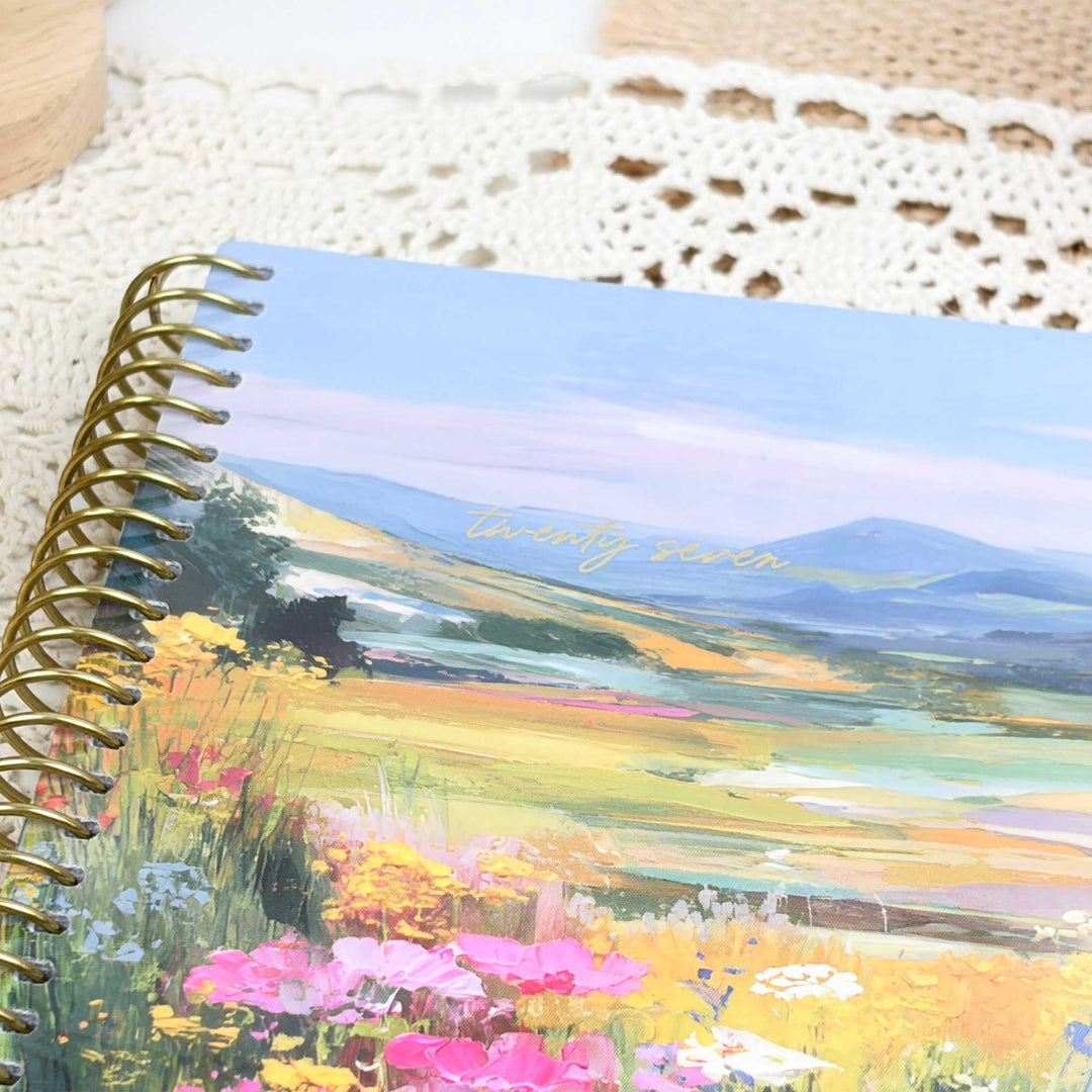 Notebook with a scenic cover featuring mountains and flowers, placed on a textured surface.