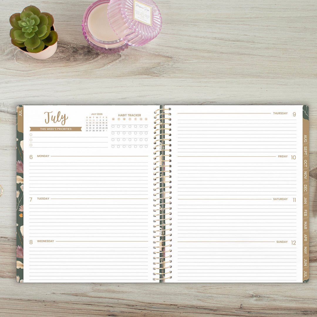 Open planner showing July calendar on a wooden surface with a plant and candle.