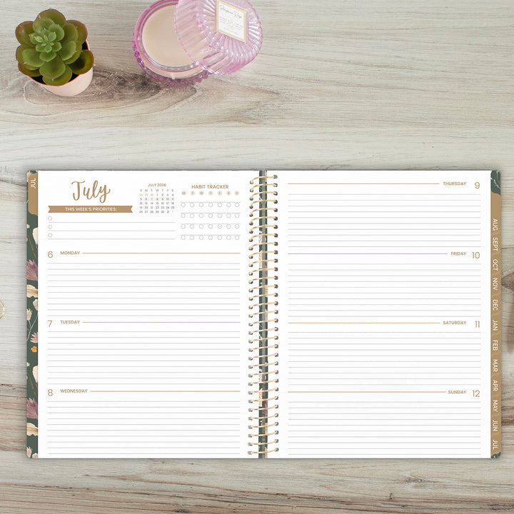Open planner showing July calendar on a wooden surface with a plant and candle.