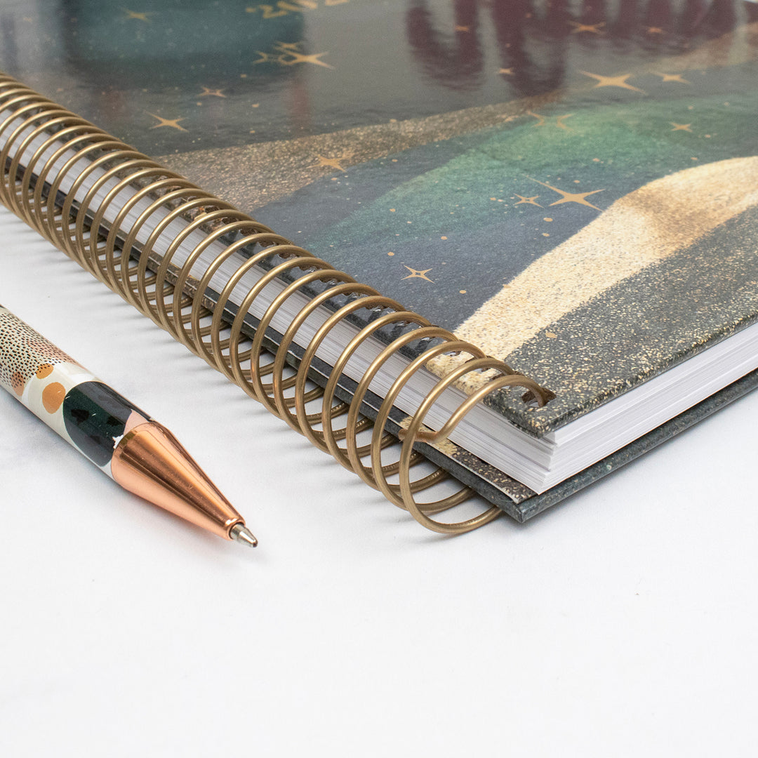 Planner with gold spiral binding and pen on a white background