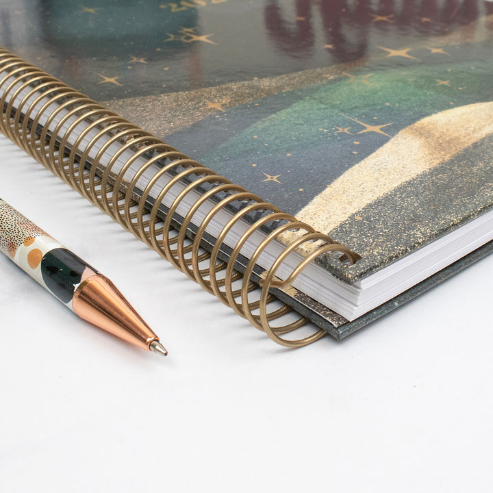 Planner with gold spiral binding and pen on a white background