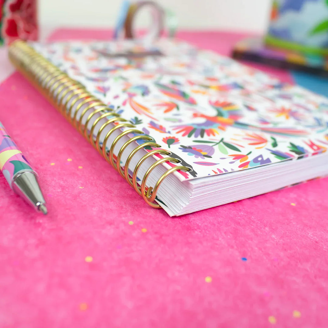 Colorful spiral-bound notebook on a pink surface with a pen next to it