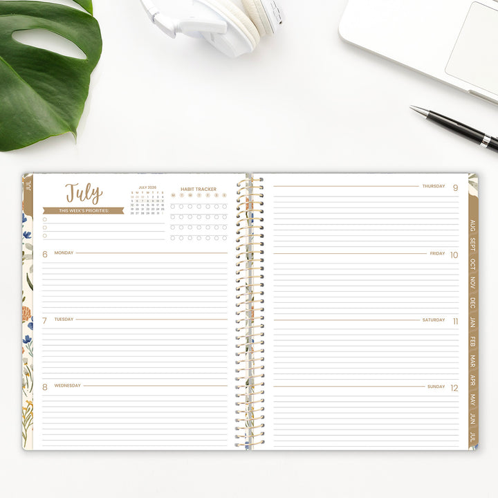 Open planner with July calendar on a white surface with a plant and pen.
