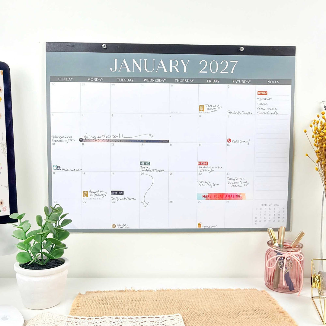 Wall calendar for January 2027 on a white wall with office supplies and decor.