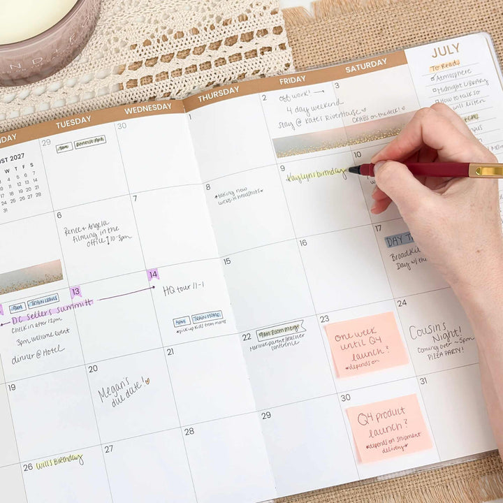 Person using a pen to mark dates on a planner with a calendar view.