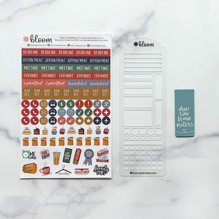 Bloom planner sticker kit laid out on a white marble background, including a main sticker sheet with colorful labels and icons, a white planner insert page, and a teal sticky note.