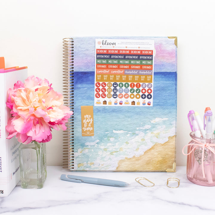 Planner with beach design on a desk with flowers and pens