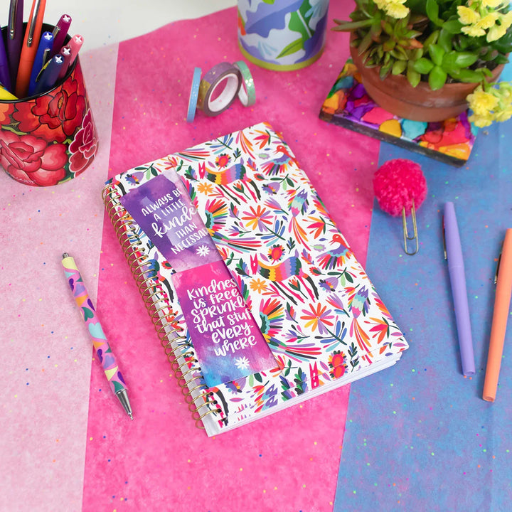 Colorful notebook with floral design on a pink and blue surface with stationery items.