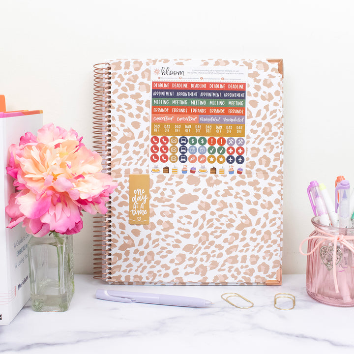 Leopard print planner with stickers on a desk with flowers and pens