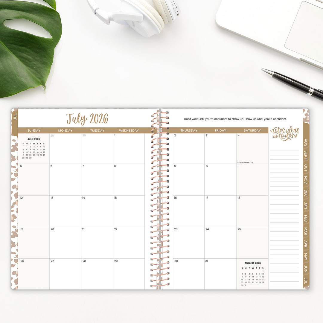 Open spiral-bound planner showing July 2026 on a white surface with a plant and pen.