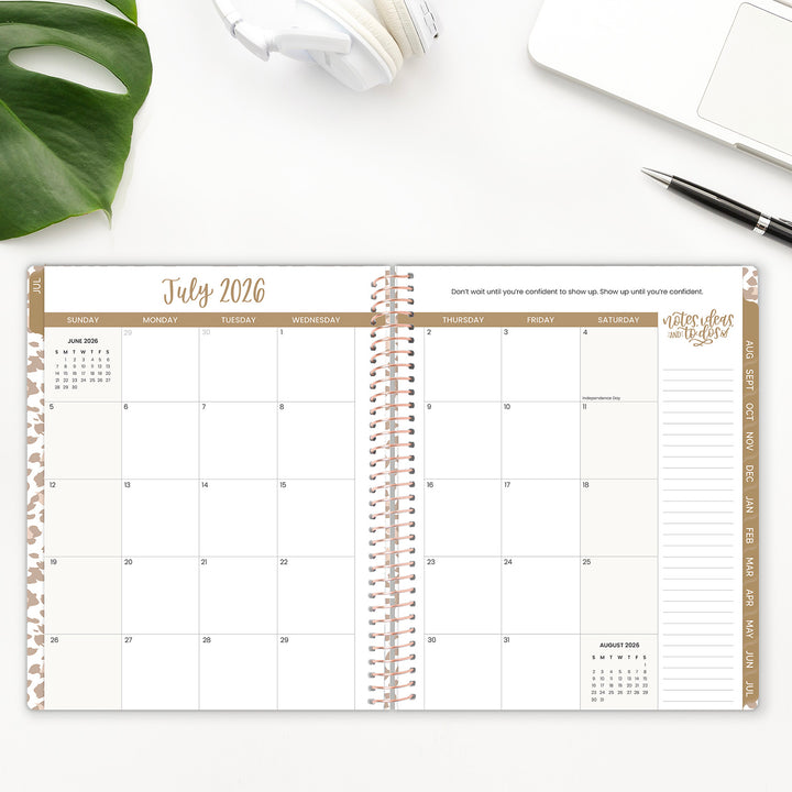 Open spiral-bound planner showing July 2026 on a white surface with a plant and pen.