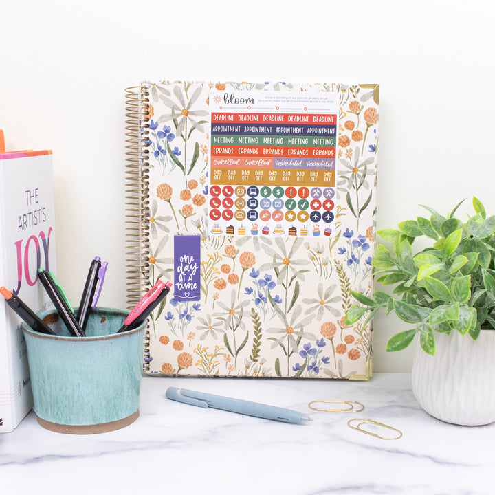 Planner with floral design on a desk with stationery items and a plant.