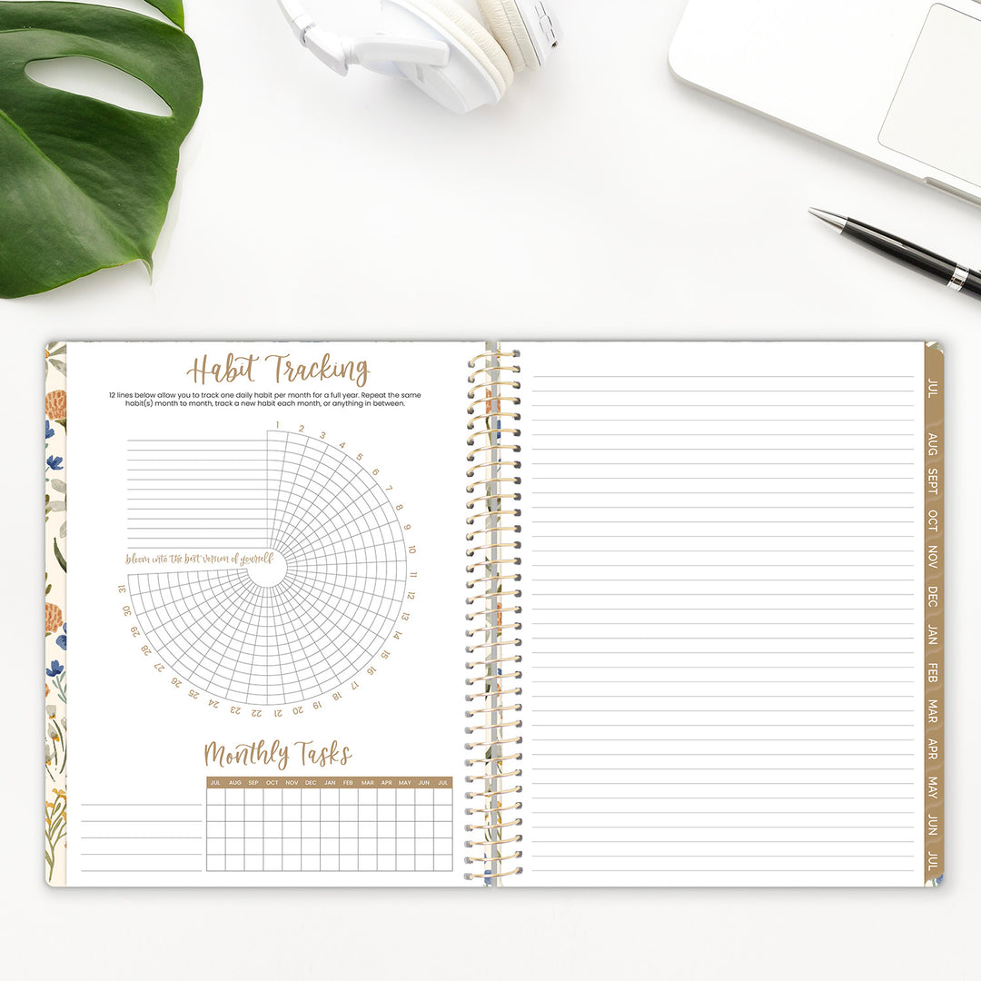 Spiral-bound planner with habit tracking and monthly tasks sections on a white surface with a plant and pen.