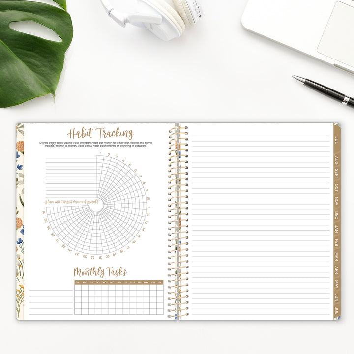 Spiral-bound planner with habit tracking and monthly tasks sections on a white surface with a plant and pen.