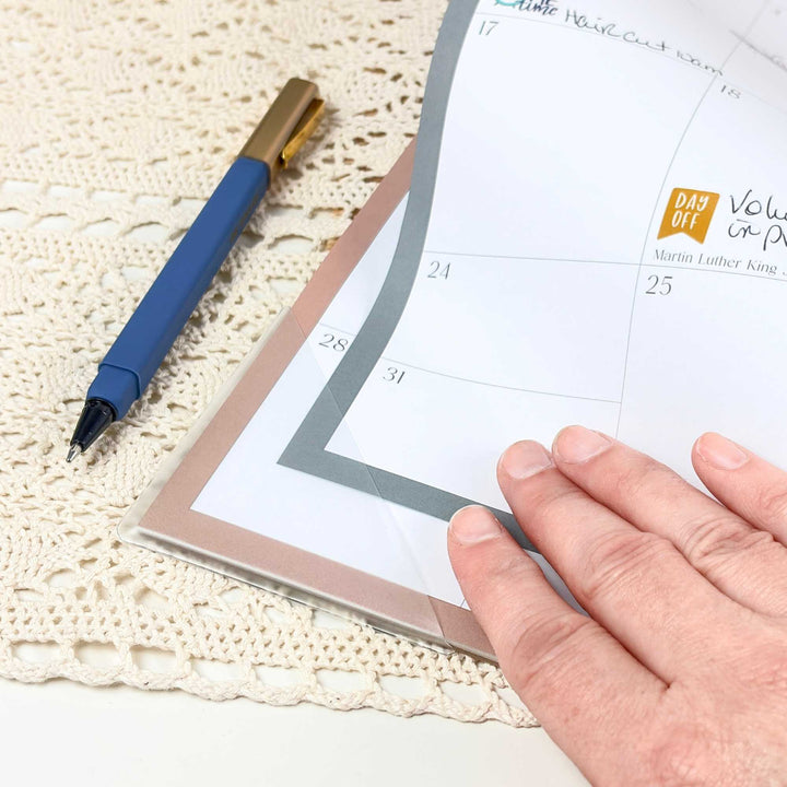 Blue pen on a calendar with a hand pointing to a date on a textured surface