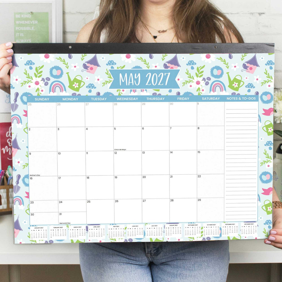 Person holding a colorful May 2027 calendar with cartoon designs.