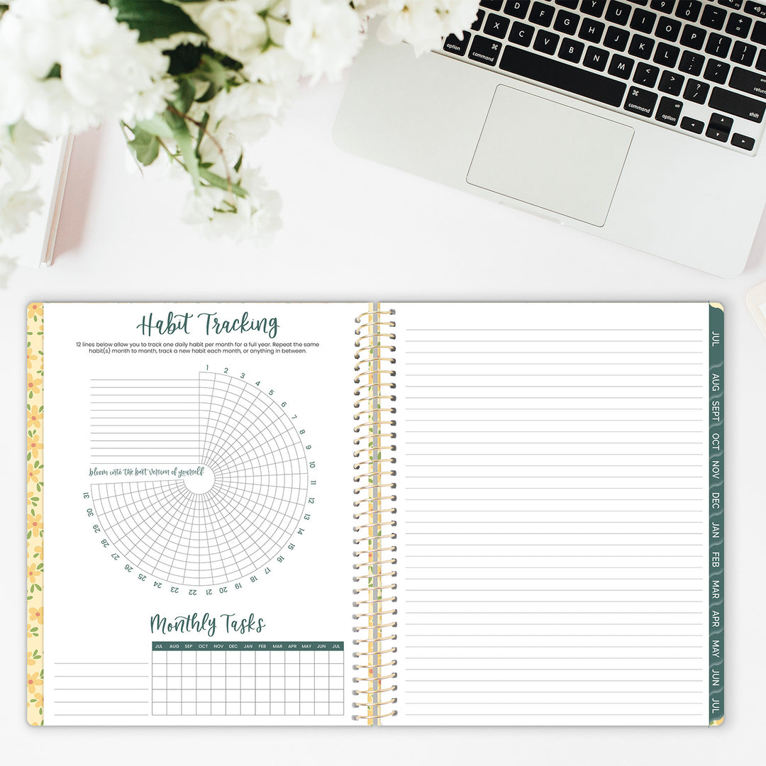 Open planner with habit tracking and monthly tasks on a desk with flowers and laptop