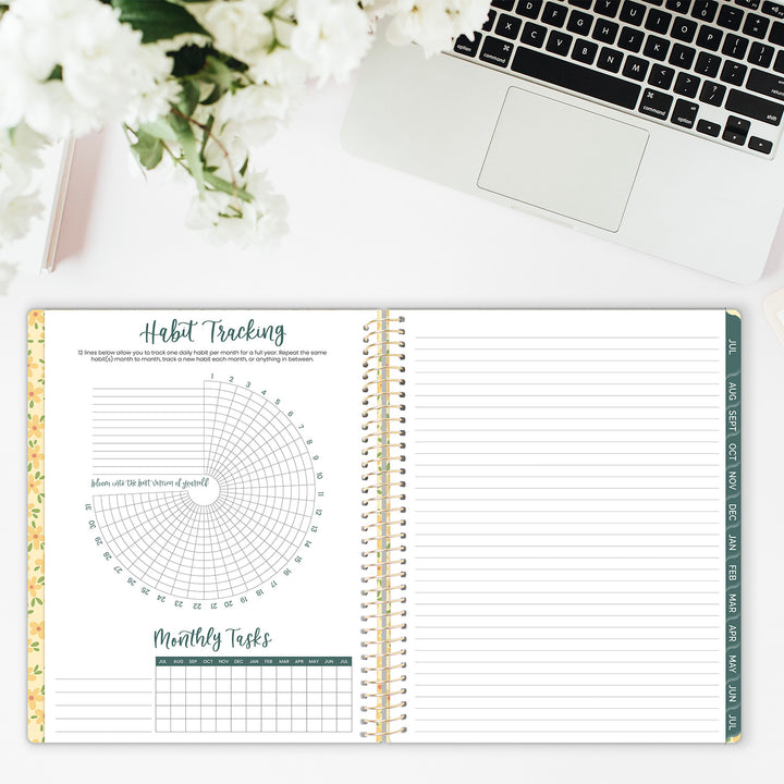 Open planner with habit tracking and monthly tasks on a desk with flowers and laptop