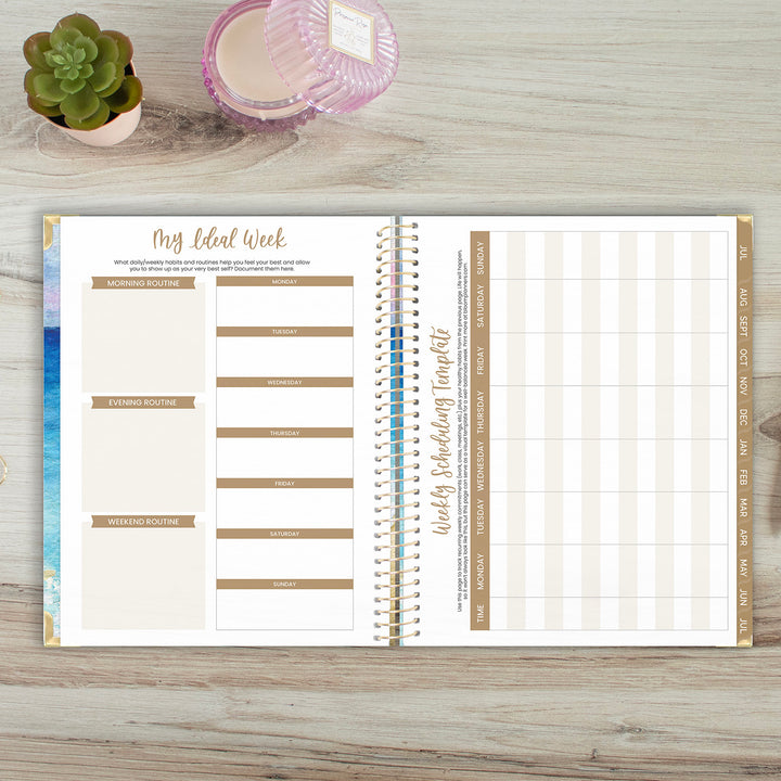 Open planner on a wooden surface with a plant and candle in the background