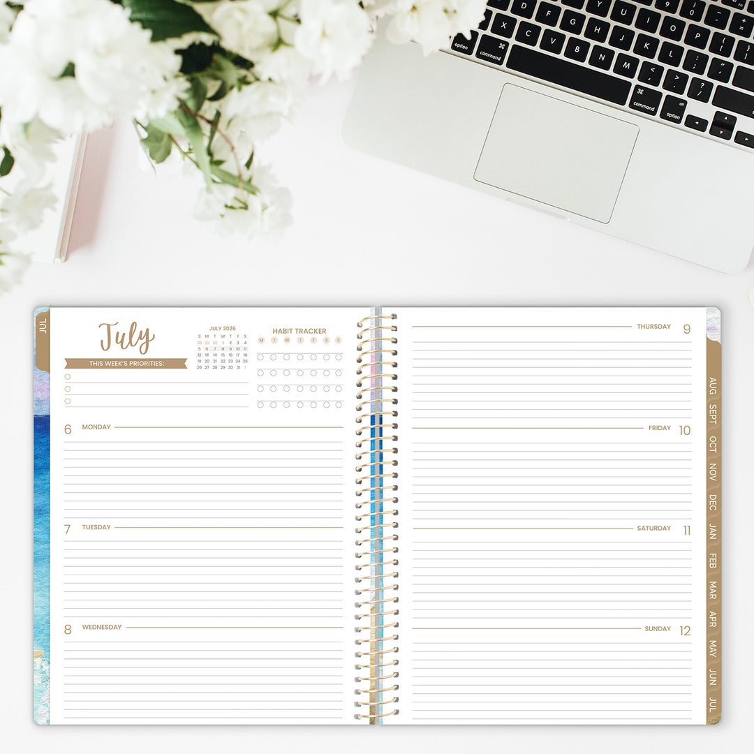 Open planner showing July calendar on a desk with flowers and laptop