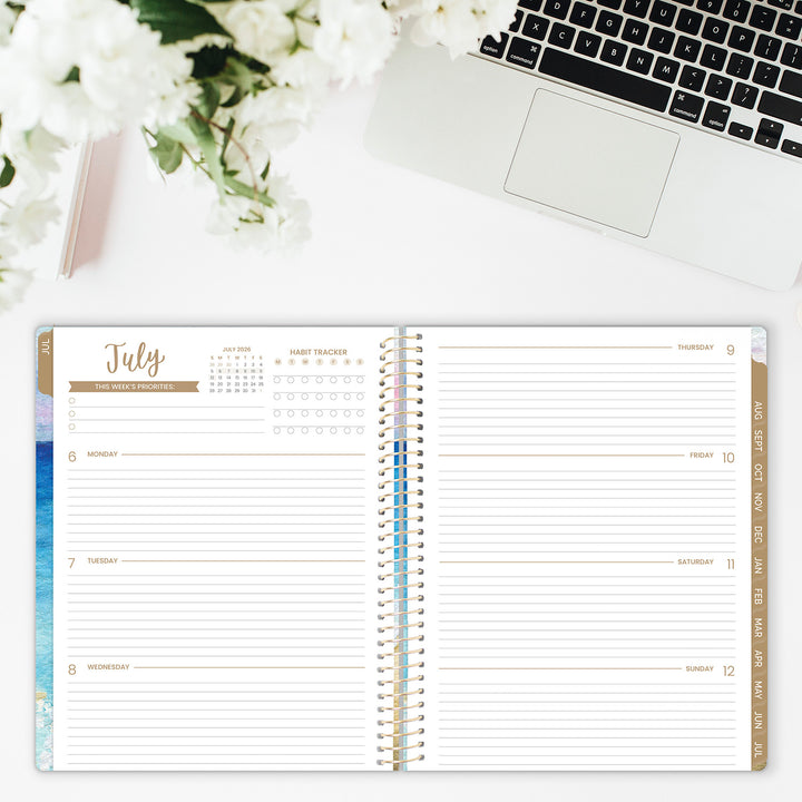 Open planner showing July calendar on a desk with flowers and laptop