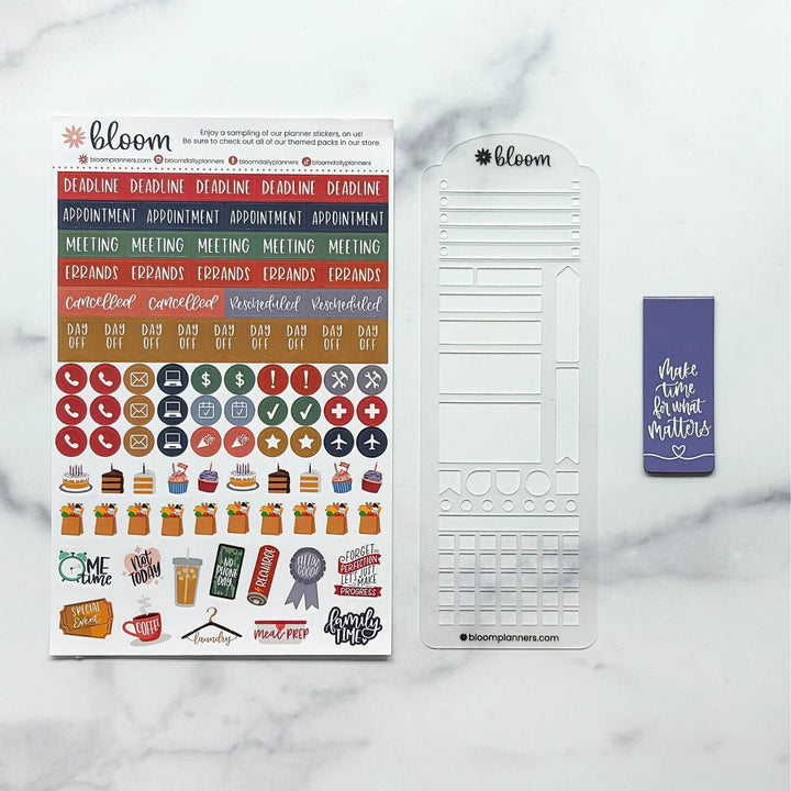 Bloom planner sticker kit and coordinating metal template set on a white marble background. The kit includes a sheet of colorful planner stickers, a white metal grid template, and a purple planner tape roll.
