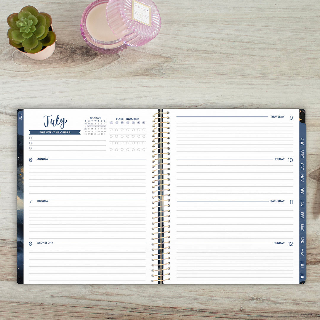 Open planner on a wooden surface with a small plant and candle