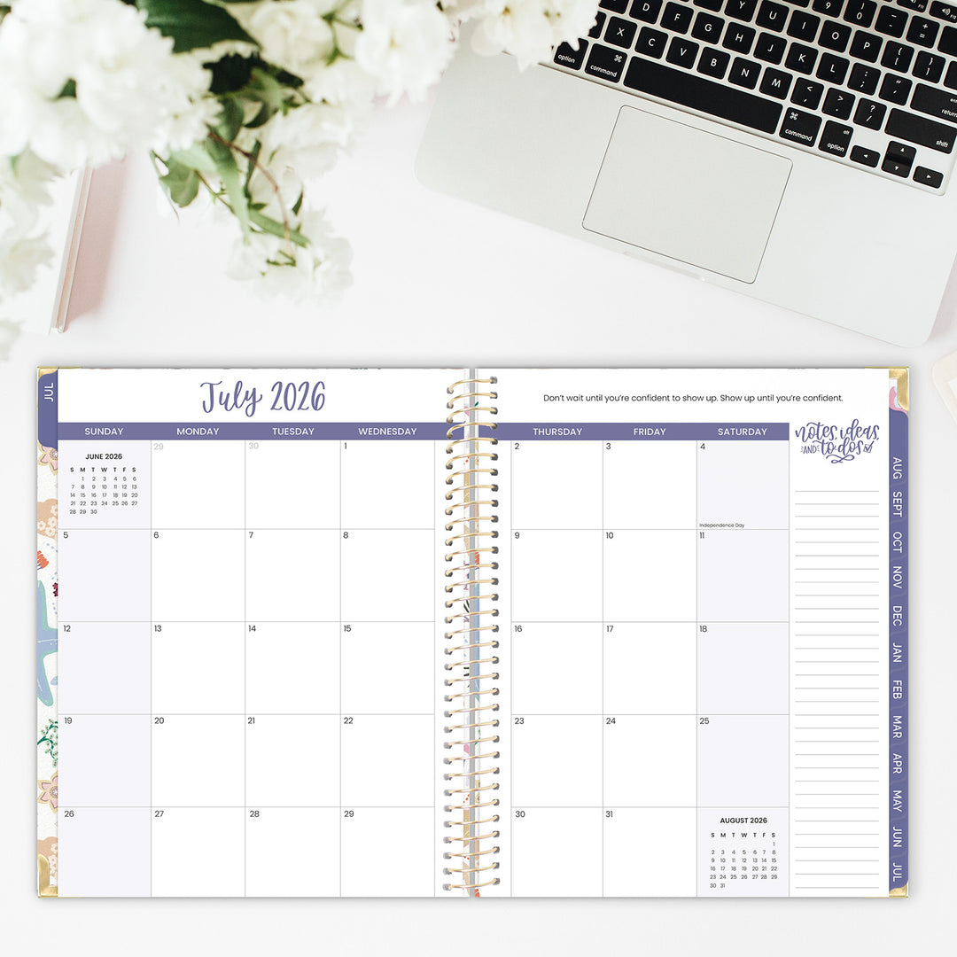 Calendar open to July 2026 on a desk with a laptop and flowers