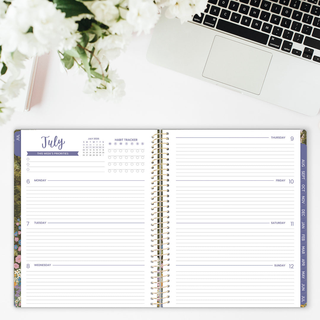 Open planner with July calendar on a desk with a laptop and flowers.